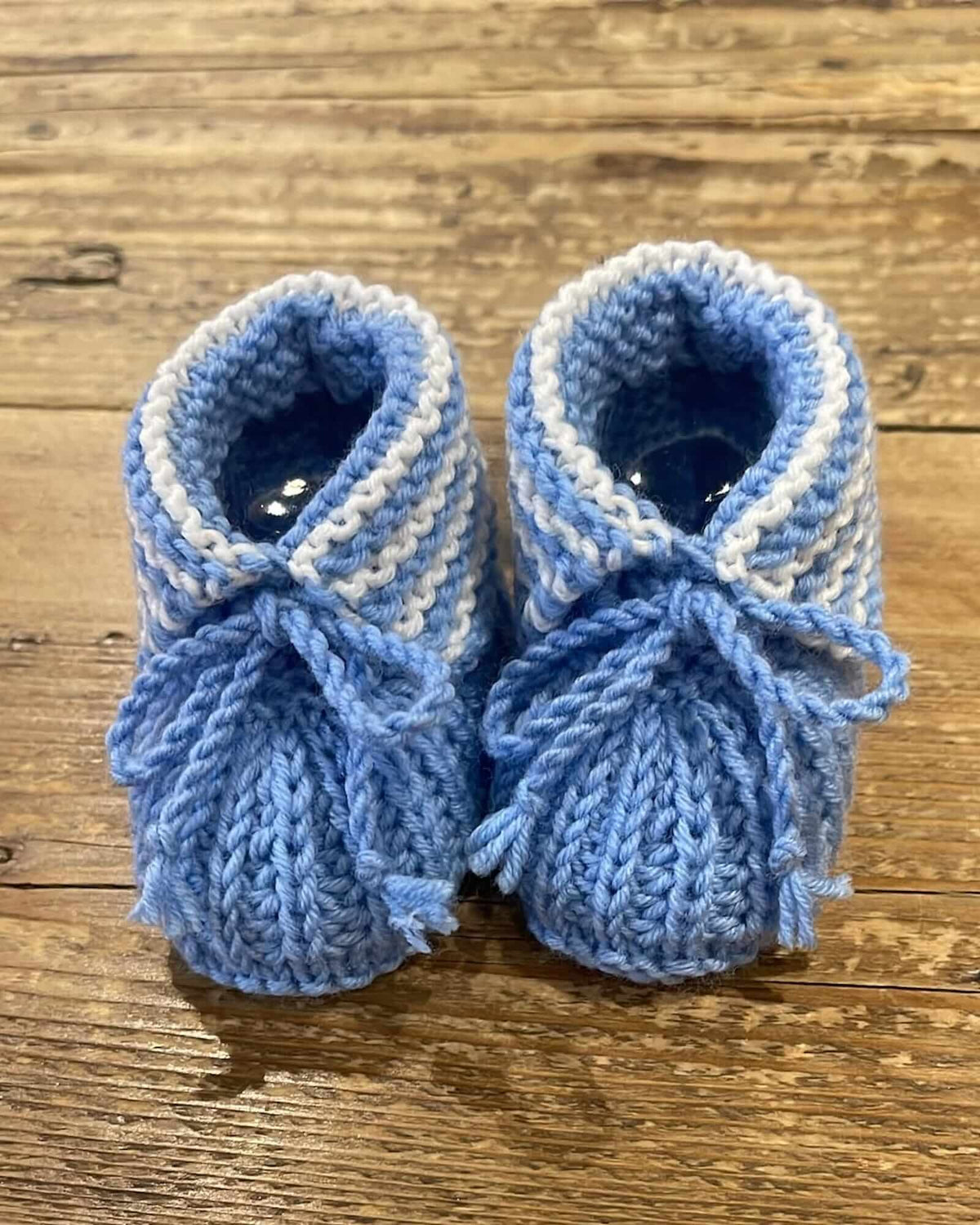 a close-up image of a pair of hand-knitted baby boots in light blue and white stripes